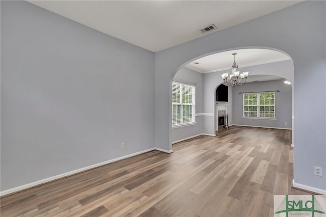 unfurnished living room featuring a textured ceiling, wood-type flooring, crown molding, and a notable chandelier