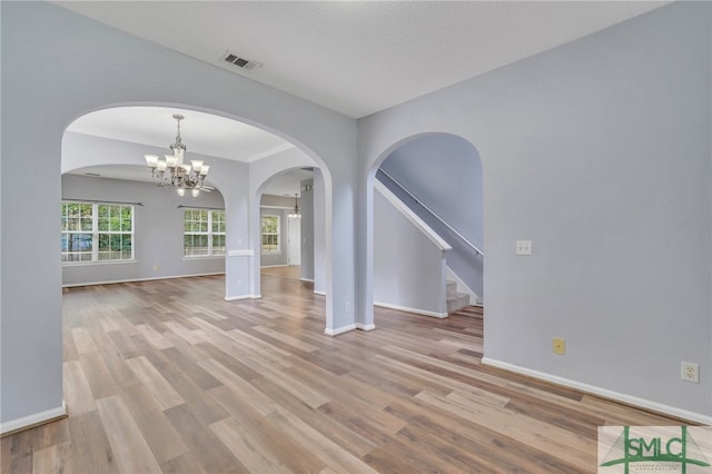 unfurnished dining area featuring light wood-type flooring, a textured ceiling, and an inviting chandelier