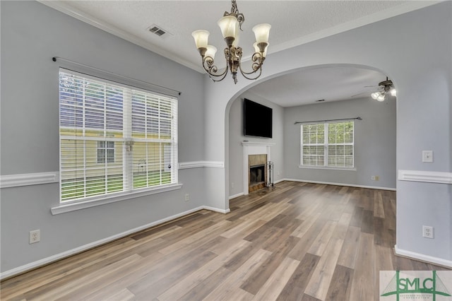 unfurnished living room with hardwood / wood-style flooring, ceiling fan with notable chandelier, a tiled fireplace, and ornamental molding