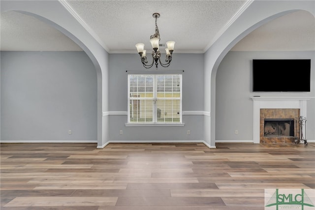 unfurnished living room featuring a textured ceiling, crown molding, an inviting chandelier, and hardwood / wood-style flooring