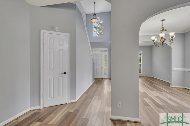 entrance foyer with wood-type flooring, a notable chandelier, crown molding, and a high ceiling