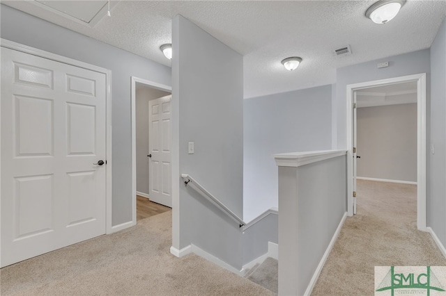 corridor with a textured ceiling and light colored carpet