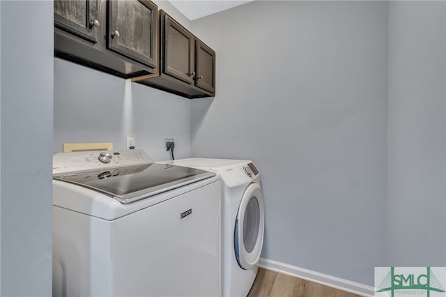 washroom featuring washing machine and clothes dryer, light hardwood / wood-style flooring, and cabinets