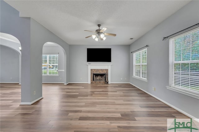 unfurnished living room featuring ceiling fan, light hardwood / wood-style flooring, plenty of natural light, and a tile fireplace