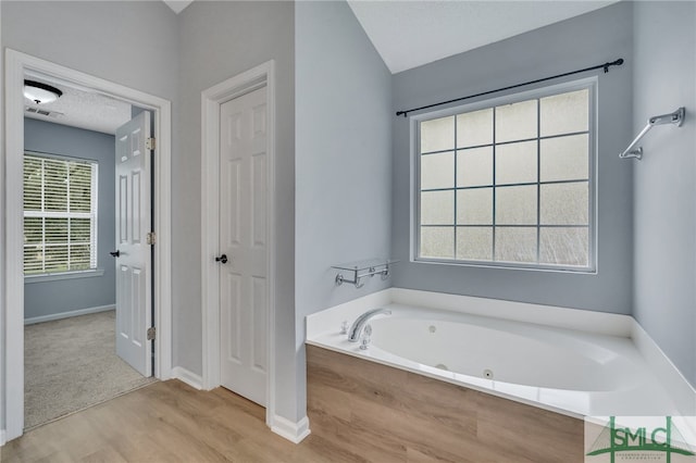 bathroom featuring a textured ceiling, a bathtub, hardwood / wood-style floors, and lofted ceiling