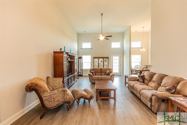 living room featuring ceiling fan with notable chandelier, light wood-type flooring, a high ceiling, and plenty of natural light