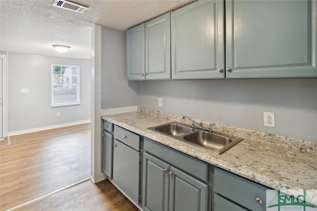 kitchen with light hardwood / wood-style flooring, a textured ceiling, gray cabinets, and sink