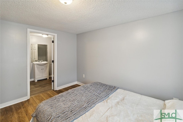 bedroom with ensuite bathroom, a textured ceiling, dark hardwood / wood-style floors, and sink