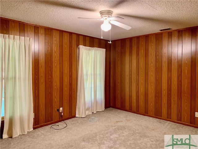 carpeted empty room featuring a textured ceiling, wood walls, and ceiling fan