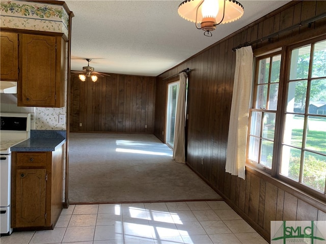 kitchen featuring white range oven, wooden walls, ceiling fan, and light colored carpet