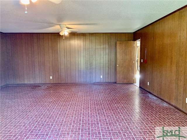 spare room featuring ceiling fan, a textured ceiling, and wood walls