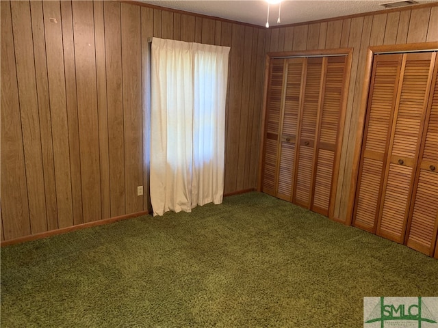 unfurnished bedroom with a textured ceiling, carpet, wooden walls, and two closets