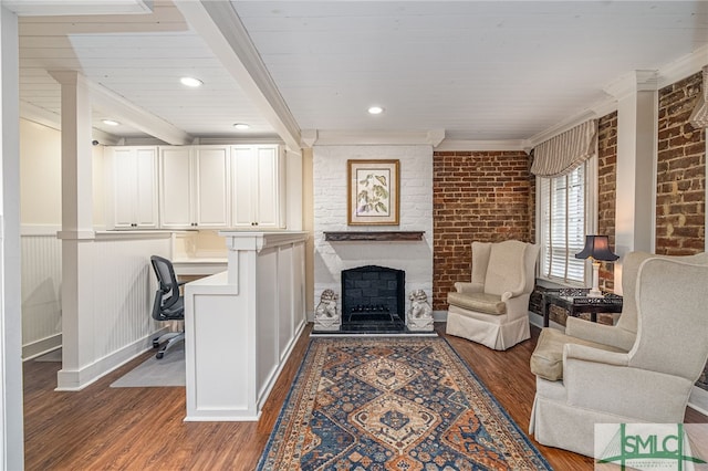 living room with beamed ceiling, built in desk, brick wall, dark hardwood / wood-style flooring, and a large fireplace