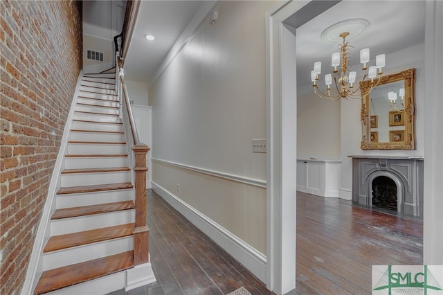 stairs featuring brick wall, a chandelier, and hardwood / wood-style floors