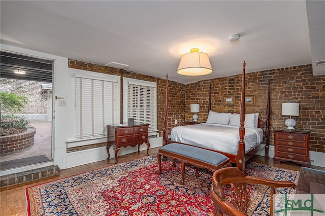 bedroom with brick wall and hardwood / wood-style flooring