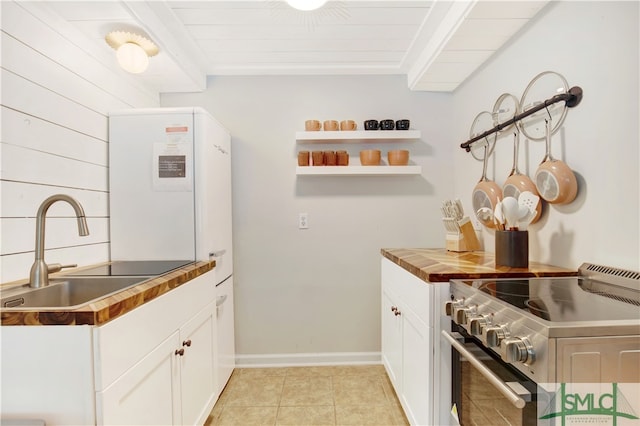 kitchen featuring wooden counters, sink, light tile patterned floors, white cabinets, and stainless steel stove