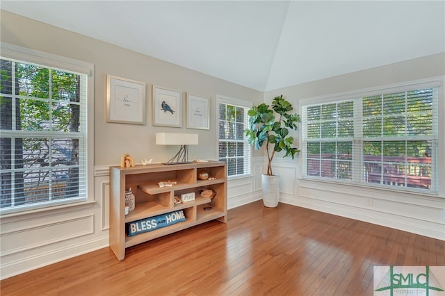 living area with a healthy amount of sunlight, lofted ceiling, and wood-type flooring