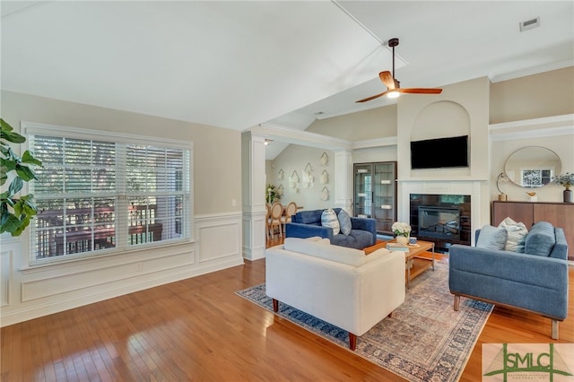 living room featuring a fireplace, ornate columns, ceiling fan, light hardwood / wood-style flooring, and ornamental molding