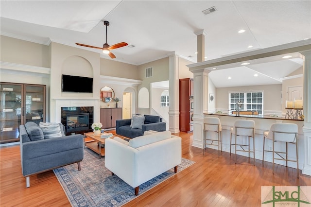 living room with light wood-type flooring, a fireplace, ceiling fan, and ornate columns