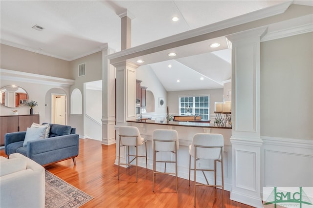 kitchen featuring vaulted ceiling, a breakfast bar, kitchen peninsula, light hardwood / wood-style flooring, and ornamental molding