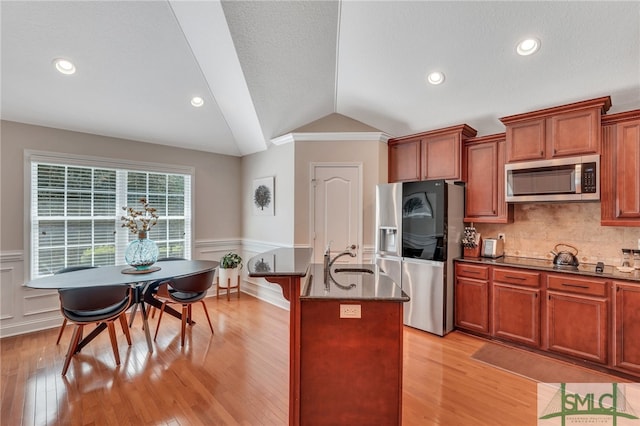 kitchen featuring light wood-type flooring, a kitchen island with sink, lofted ceiling, decorative backsplash, and appliances with stainless steel finishes