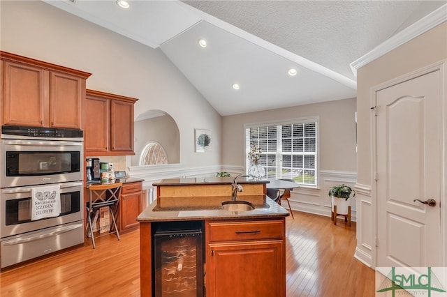 kitchen featuring vaulted ceiling, an island with sink, wine cooler, stainless steel double oven, and sink