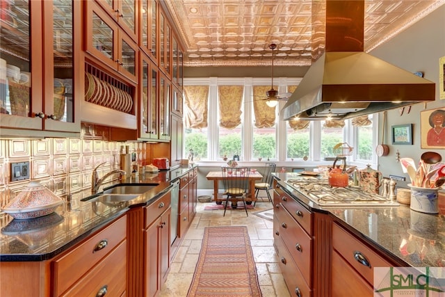 kitchen with dark stone countertops, island range hood, stainless steel appliances, decorative light fixtures, and sink