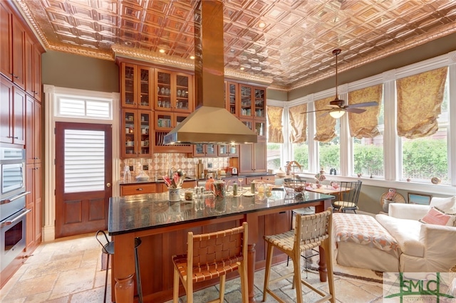 kitchen featuring tasteful backsplash, island range hood, oven, ceiling fan, and dark stone counters