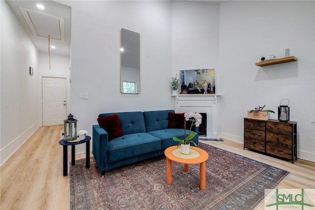 living area with a fireplace, a towering ceiling, attic access, wood finished floors, and baseboards