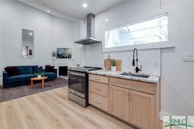 kitchen featuring light hardwood / wood-style floors, stainless steel electric stove, wall chimney exhaust hood, light brown cabinets, and sink