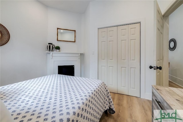 bedroom with light wood-style floors, a fireplace, and a closet