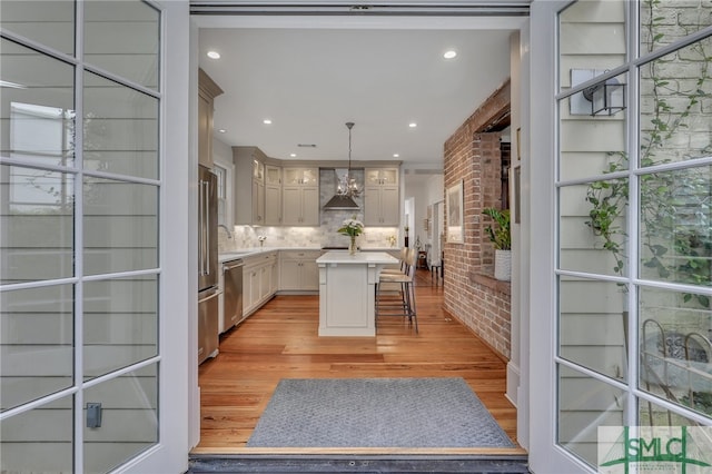 kitchen with hanging light fixtures, wall chimney exhaust hood, stainless steel appliances, a center island, and a breakfast bar area