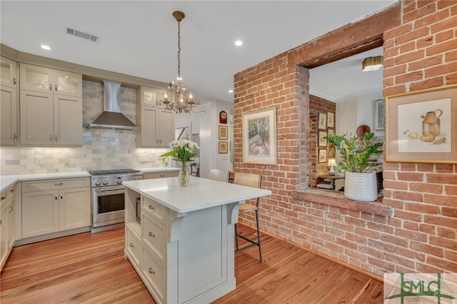 kitchen featuring a kitchen island, high end stainless steel range, wall chimney exhaust hood, a breakfast bar area, and light hardwood / wood-style floors