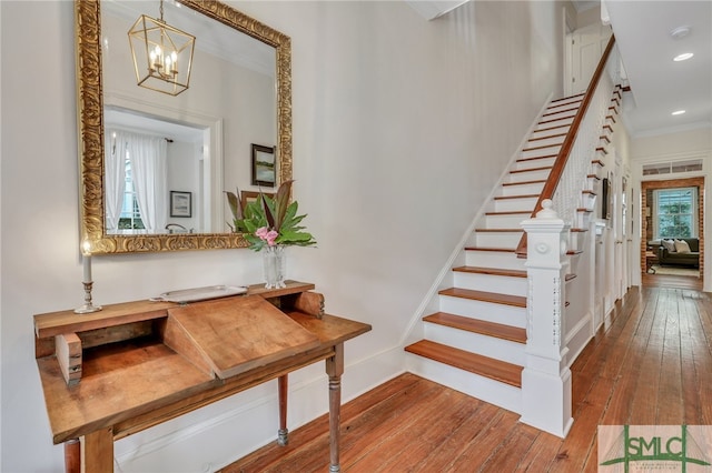 stairs with wood-type flooring, crown molding, and a chandelier