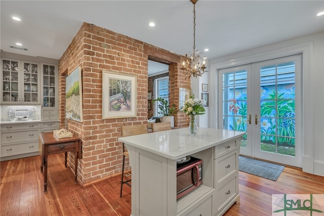 kitchen with white cabinets, hanging light fixtures, french doors, light hardwood / wood-style flooring, and a center island