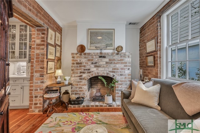 sitting room with a brick fireplace, light wood-type flooring, crown molding, and brick wall