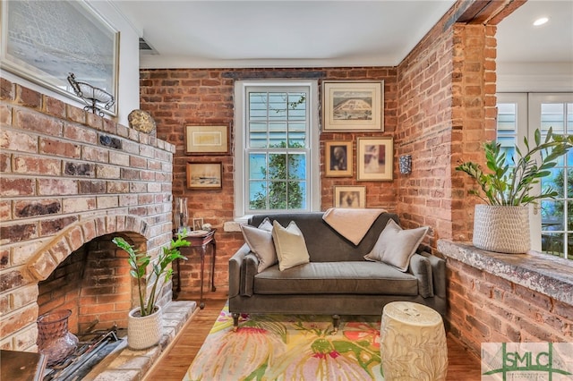 living area featuring wood-type flooring, a brick fireplace, and brick wall