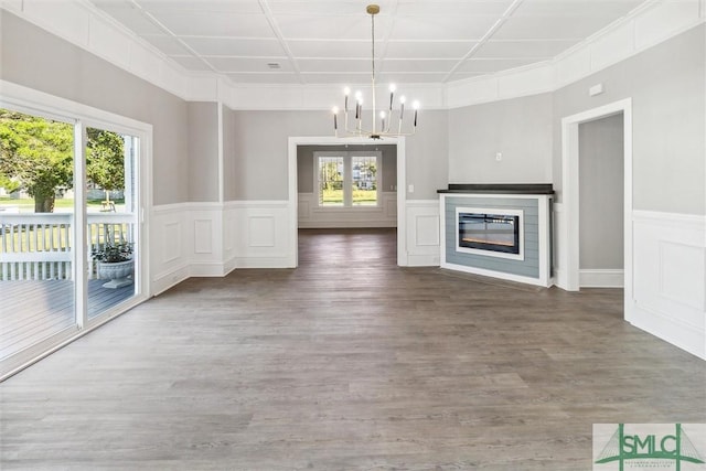 unfurnished living room featuring a decorative wall, an inviting chandelier, a glass covered fireplace, a wainscoted wall, and wood finished floors
