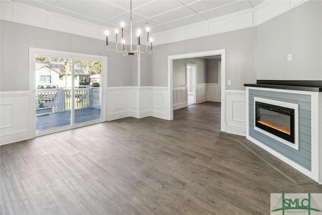 unfurnished living room with dark wood-style flooring, a decorative wall, a notable chandelier, and a glass covered fireplace