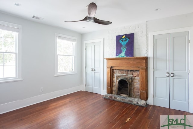 unfurnished living room with ceiling fan, dark wood-type flooring, and a stone fireplace