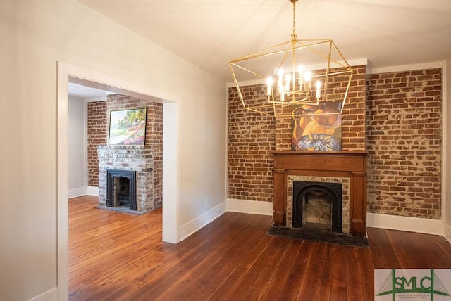 unfurnished living room featuring a notable chandelier, a brick fireplace, brick wall, and hardwood / wood-style flooring