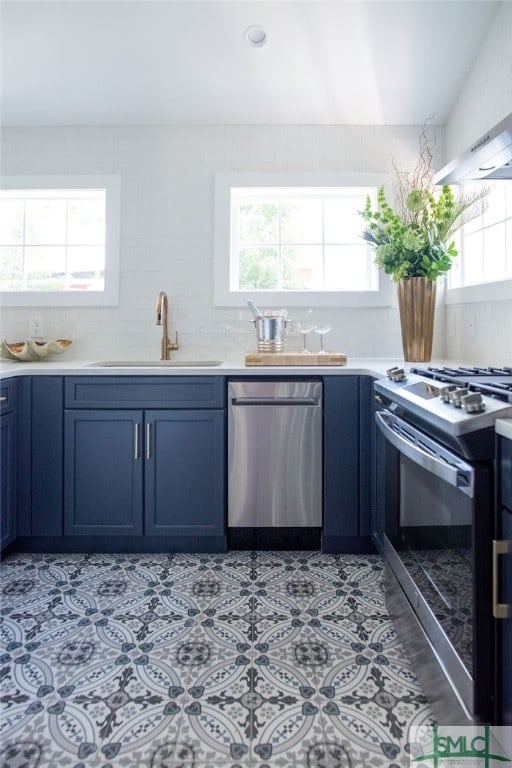 kitchen featuring blue cabinets, tasteful backsplash, sink, stainless steel appliances, and exhaust hood