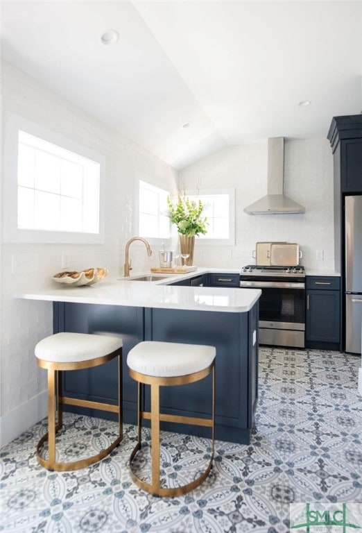 kitchen featuring appliances with stainless steel finishes, kitchen peninsula, wall chimney exhaust hood, and a breakfast bar