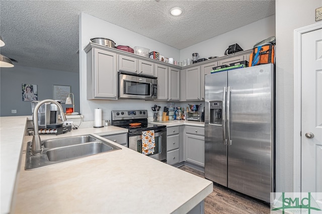 kitchen with a textured ceiling, appliances with stainless steel finishes, dark wood-type flooring, and sink