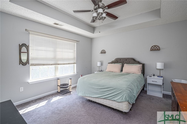 carpeted bedroom with ceiling fan, a textured ceiling, and a tray ceiling