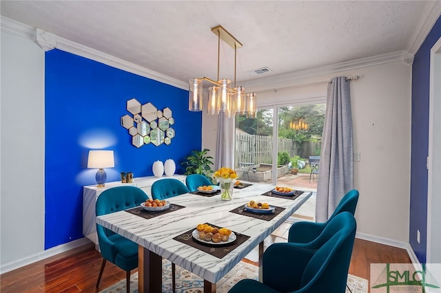 dining area featuring an inviting chandelier, crown molding, wood finished floors, and visible vents