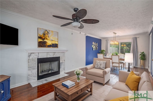 living room with ornamental molding, wood finished floors, baseboards, a textured ceiling, and ceiling fan with notable chandelier