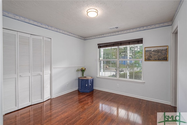 unfurnished bedroom featuring a textured ceiling, visible vents, hardwood / wood-style flooring, baseboards, and a closet