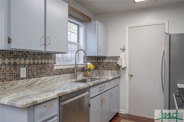 kitchen featuring appliances with stainless steel finishes, sink, dark wood-type flooring, light stone counters, and decorative backsplash