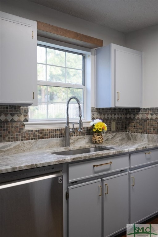 kitchen featuring stainless steel dishwasher, white cabinets, a sink, and tasteful backsplash